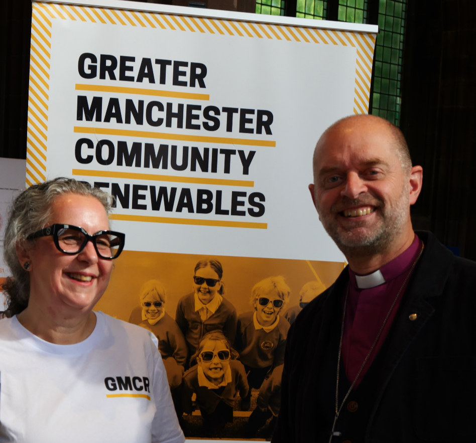 Photograph of GMCR volunteers Sarra and Manchester Cathedral's Bishop smiling in front of a GMCR banner